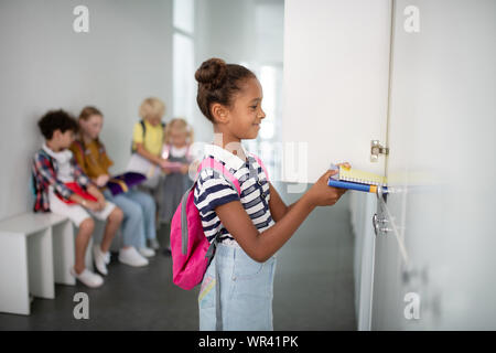 Sorridente di carnagione scura ragazza mettendo libri raccoglitore interno Foto Stock