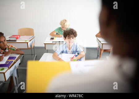 Curly dai capelli scuri cerca ragazzo al maestro durante la lezione Foto Stock