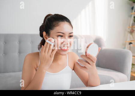 Ritratto di una bellezza giovane donna cosmetici guardando nello specchio usando una spugna con polvere. Foto Stock