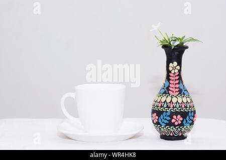 Casa interni stile di design interno con tazza di argilla bianca Cina e vaso artistico in argilla nera fiore in primo piano con sfondo bianco per carta da parati Foto Stock