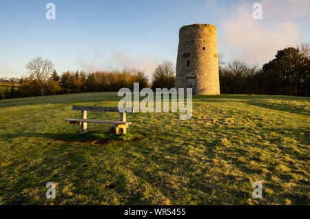 Resti di una torre mulino a vento in una collina erbosa con una sede in legno in primo piano Foto Stock