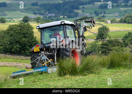 Topping erba ricoperta su un altopiano di pascolo con un trattore Hurlimann e un pascolo di Fleming topper. North Yorkshire, Regno Unito. Foto Stock