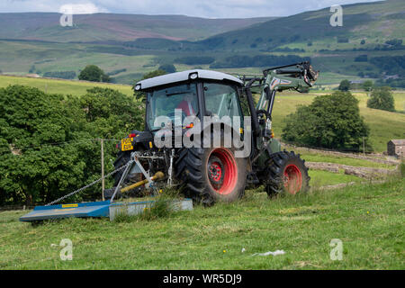 Topping erba ricoperta su un altopiano di pascolo con un trattore Hurlimann e un pascolo di Fleming topper. North Yorkshire, Regno Unito. Foto Stock