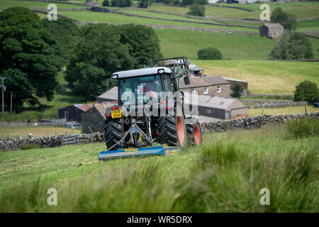 Topping erba ricoperta su un altopiano di pascolo con un trattore Hurlimann e un pascolo di Fleming topper. North Yorkshire, Regno Unito. Foto Stock