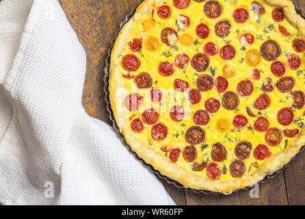 Pomodoro ciliegino quiche con uovo e ripieno di formaggio in una teglia da forno con il canovaccio sul tavolo di legno - vista superiore foto Foto Stock