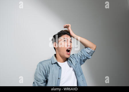 Ritratto di un uomo asiatico tenendo la sua testa con la mano e che soffrono di mal di testa in un paio di jeans t-shirt su sfondo bianco Foto Stock