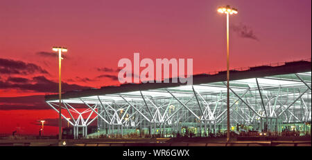 Crepuscolo e luci accese a Londra Stansted Airport terminal passeggeri costruzione telaio spazio completato nel 1991 breve rosso fuoco tramonto cielo Essex Inghilterra UK Foto Stock