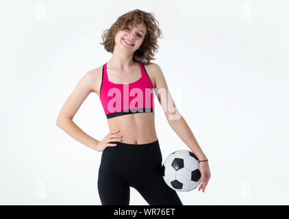 Sport giovane donna con un pallone da calcio nelle sue mani in piedi su uno sfondo grigio. Giocare a calcio femminile. Foto Stock