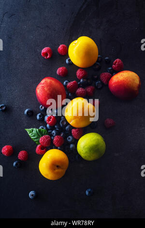 Creative flatlay con frutta fresca e bacche su sfondo scuro. Le uve, mirtilli e lamponi con pesche e calce Foto Stock