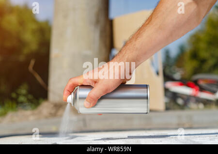 Maschio di mano impugna uno spray per aerosol può, disegna graffiti su asfalto Foto Stock