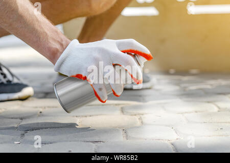 Maschio in mano un guanto contiene un aerosol spray può con vernice bianca, colori. Verniciatura superficiale, i graffiti sulla strada. Foto Stock