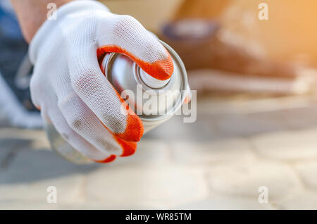 Maschio in mano un guanto contiene un aerosol spray può con vernice bianca, colori. Verniciatura superficiale, i graffiti sulla strada. Foto Stock