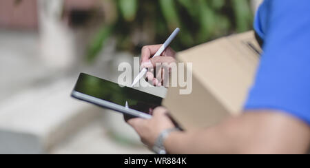 Vista ravvicinata di consegna professionale uomo che lavora con casella di pacchi mentre si verifica l'ordine del cliente su tablet Foto Stock