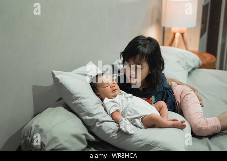 Vecchia sorella gioca con piccola sorella sul letto Foto Stock