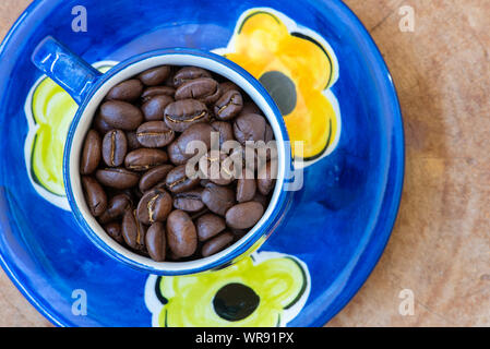 I chicchi di caffè in un dipinto a mano e tazza piattino disposti su un sfondo di legno. Foto Stock