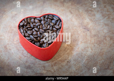 I chicchi di caffè in un cuore-stagno sagomati disposti su un sfondo di legno. Foto Stock