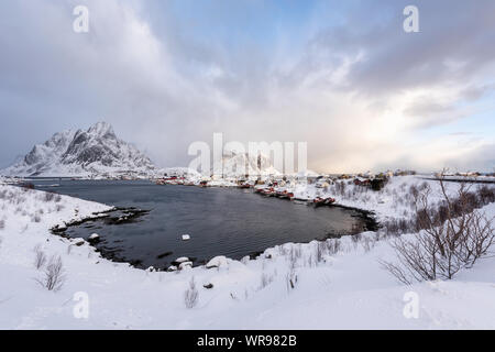 Bellissimo villaggio di Reine nelle Isole Lofoten in Norvegia. Coperta di neve paesaggio invernale al tramonto. Straordinaria attrazione turistica in circolo polare. Panora Foto Stock