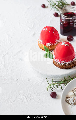 Mousse di moda la torta con la glassa a specchio e ciliegia riempimento su un cuscino di noci di cocco biscotti con scaglie di noce di cocco. Moderno e dessert. Foto Stock