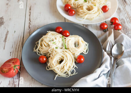 La pasta italiana spaghetti nidifica su un bianco piastra di porcellana con pomodori, parmigiano e livelli di foglie di rucola. Foto Stock