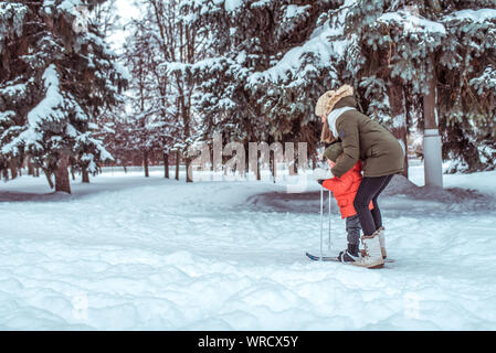 Una giovane madre insegna poco figlio un bambino di 3-5 anni, sci per i bambini, in inverno nei boschi, in vacanza, un resort nel parco innevato, sfondo Foto Stock