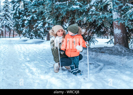 Una giovane madre insegna un piccolo figlio di un bambino di 3-5 anni, sci per i bambini, in inverno nel bosco, in vacanza, un resort in un parco innevato Foto Stock