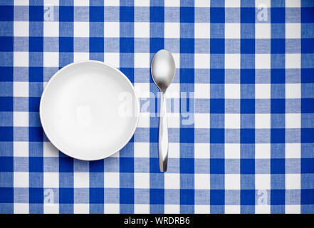 Bianco vuoto ciotola e cucchiaio su un blu tovaglia gingham Foto Stock