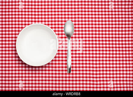 Bianco vuoto ciotola e cucchiaio su un rosso Gingham tovaglia Foto Stock