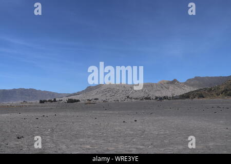 Chiudere fino al bromo cratere Batok vicino vulcano. Mare di sabbia nera e ceneri in bromo caldera valley. Cielo sereno e soleggiato fondovalle con i vulcani. Foto Stock