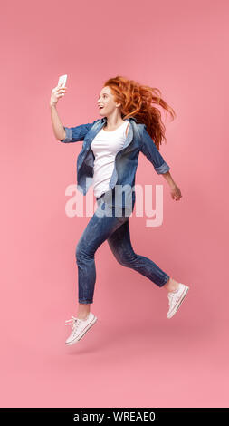 La millenaria Redhead Girl Jumping e utilizzando il telefono, Foto Stock