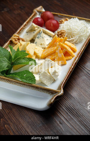 Bella impostazione tabella piatto di formaggio su una piastra bianca su sfondo scuro. Cibo per lo styling. Il menu del ristorante Foto Stock