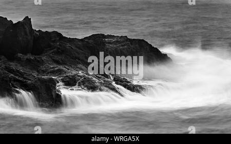 Una lunga esposizione della vista di dettaglio degli alti spruzzi delle onde di colpire le rocce con piccole cascate a Playa de Nogales in La Palma, Spagna. Foto Stock