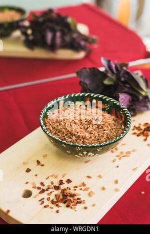 Zira riso consiste in una piastra orientali. riso scuro giace su un sfondo orientali, una tovaglia dorata, un tagliere di legno accanto al basilico Foto Stock