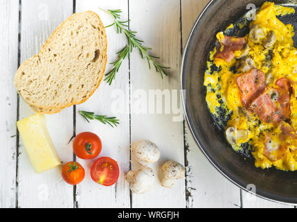 Frittata con pancetta e funghi sul tavolo bianco. Pomodori ciliegini, formaggio e rosmarino come decorazione. Elevato angolo di visione Foto Stock