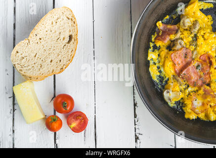 Frittata con pancetta e funghi sul tavolo bianco. Pomodori ciliegini, formaggio e rosmarino come decorazione. Elevato angolo di visione Foto Stock