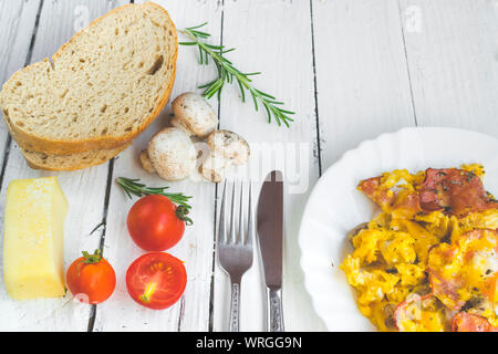 Frittata con pancetta e funghi sul tavolo bianco. Pomodori ciliegini, formaggio e rosmarino come decorazione. Elevato angolo di visione Foto Stock