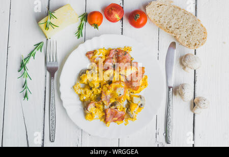 Frittata con pancetta e funghi sul tavolo bianco. Pomodori ciliegini, formaggio e rosmarino come decorazione. Elevato angolo di visione Foto Stock