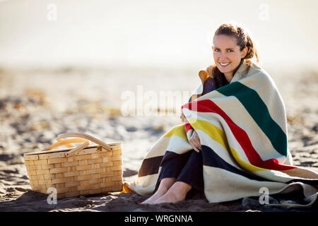 Ritratto di un sorridente giovane donna avvolta in una coperta di grandi dimensioni presso la spiaggia. Foto Stock