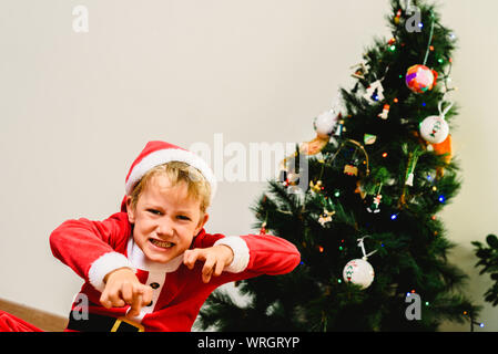 Il Toddler boy con divertente faccia indossando il costume di Santa cercando di spaventare come il Grinch, espressioni e concetti di natale isolato su sfondo bianco. Foto Stock