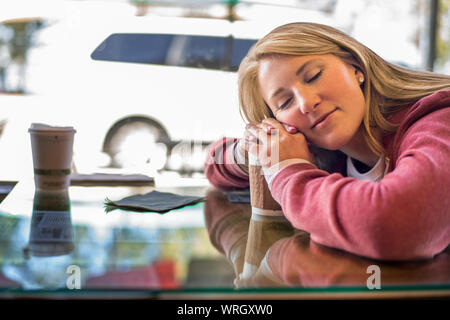 Stanco giovane donna appoggiato la sua testa sulla sua tazza di caffè. Foto Stock