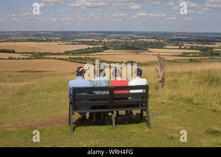 Famiglia di quattro sedersi sulla panchina ammirando vista collina a Whipsnade sulla calda mattina d'estate Foto Stock