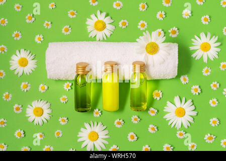 Piatto di laici piccolo mockup bottiglie con spa prodotti cosmetici su sfondo verde con freschi Fiori di camomilla. Le donne di bellezza e un salone di bellezza cosmetici Foto Stock