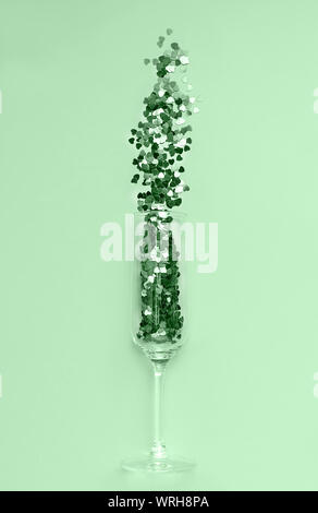 Alla moda di menta neo a forma di cuore coriandoli versata al di fuori del bicchiere di champagne. Amore e celebrazione del concetto. Lay piatto. Foto Stock