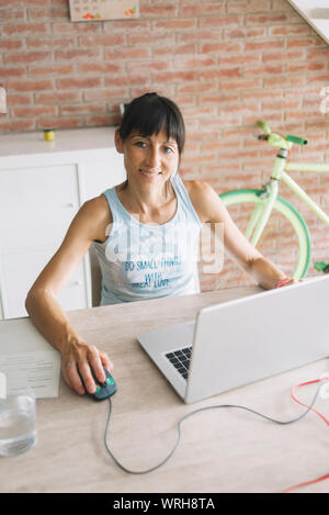 Donna sorridente con notebook di lavoro a casa mentre guardando la fotocamera Foto Stock