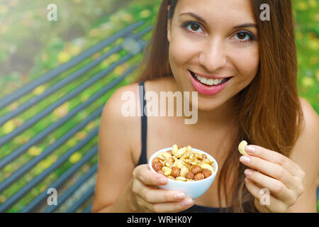 Close up sorridente ragazza mangiando snack mix di dadi seduta nel parco. Foto Stock