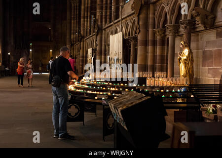 Un uomo accende un cero della preghiera presso la cattedrale di Notre Dame a Strasburgo, Grand Est, Francia. Foto Stock