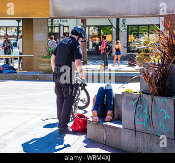 Un funzionario di polizia su una bicicletta a parlare con una donna Bevuto a Seattle il Westlake Park Foto Stock