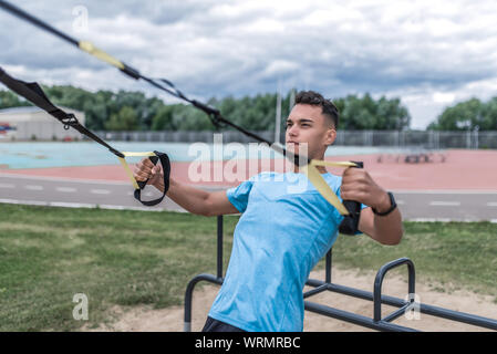 Athletic uomo atleta sulla formazione di loop, cinghie attiva la trazione, estate città formazione, motivazione per fare sport fitness workout. Uno stile di vita attivo Foto Stock