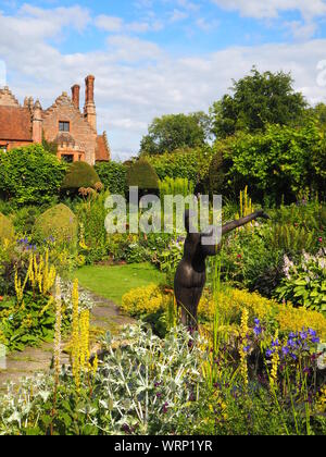 Ritratto di Chenies Manor House e affondata giardino, stagno ornamentale con Alan Biggs' SCULTURA;f affilatura pianta verde frontiera nel tardo pomeriggio di sole in giugno. Foto Stock