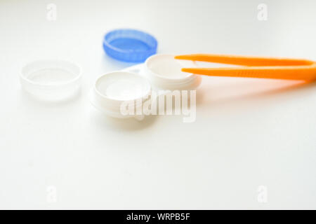 Accessori per l'uso corretto delle lenti a contatto: Custodia e pinzette arancioni su sfondo bianco chiaro. Correzione sicura della visione. Messa a fuoco selettiva. Foto Stock