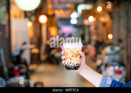 Ragazza giovane è in attesa e che mostra una tazza di zucchero di canna aromatizzato tapioca pearl bubble latte tè nella notte di mercato di Taiwan sfondo, vicino bokeh di fondo Foto Stock